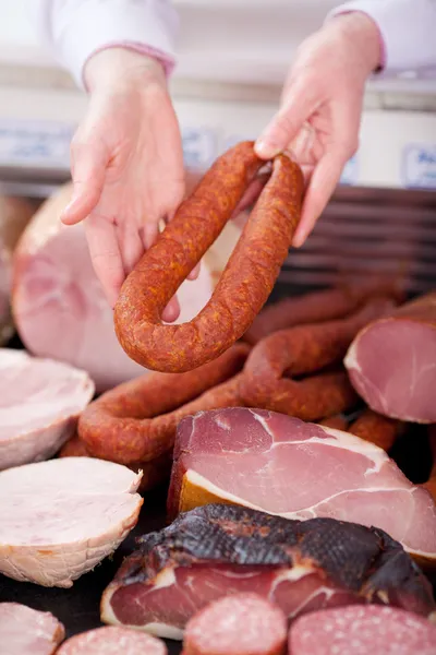 Рука мясника показывает колбасу в магазине — стоковое фото
