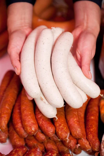 Mãos de açougueiro exibindo punhado de salsichas brancas — Fotografia de Stock