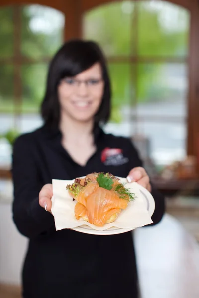 Smiling waitress displaying salmon dish — Stock Photo, Image