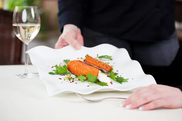 Garçonete servindo prato de salmão decorado com salsa na mesa — Fotografia de Stock