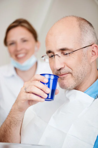 Paciente que enjuaga la boca con el dentista en el fondo en la clínica —  Fotos de Stock