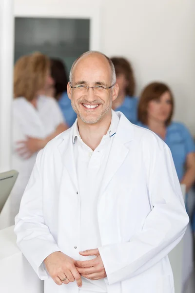 Чоловік стоматолог посміхається з помічниками на задньому плані — стокове фото