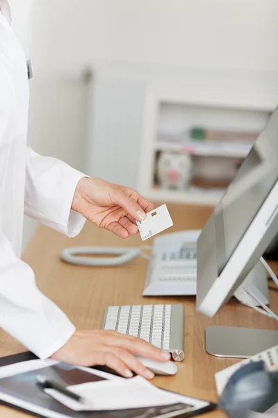 Recepcionista Segurando o cartão de identificação ao usar o computador na recepção — Fotografia de Stock