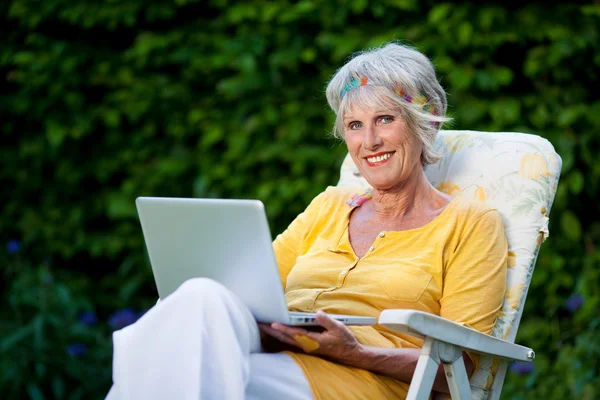 Oudere dame met behulp van laptop in de tuin — Stockfoto