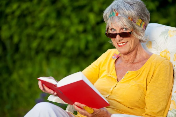 Mulher sênior olhando sobre óculos de sol durante a leitura — Fotografia de Stock