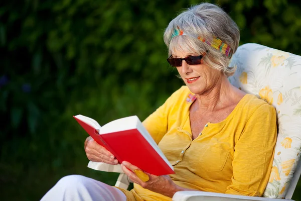 Dame âgée lisant un livre avec des lunettes de soleil — Photo