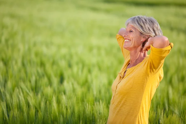 Donna anziana con le mani dietro la testa sul campo erboso — Foto Stock