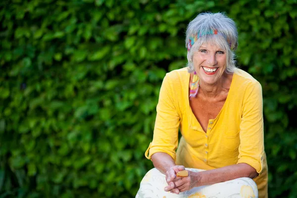 Seniorin sitzt im Park gegen Schlingpflanzen — Stockfoto