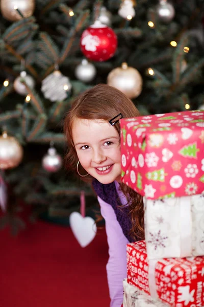 Menina brincalhão olhando em torno de presentes empilhados — Fotografia de Stock