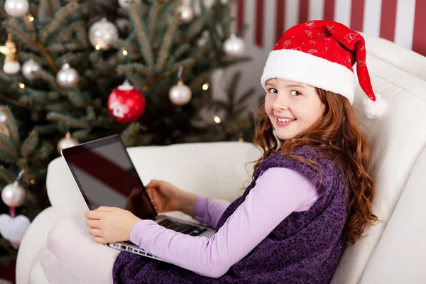 Chica sonriente en un sombrero de Santa con un ordenador portátil — Foto de Stock