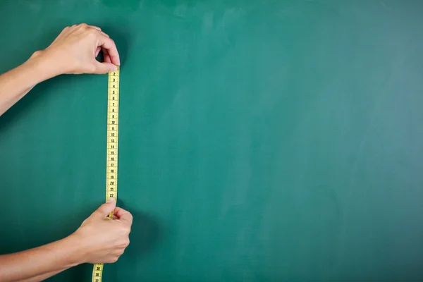 Woman's hands measuring blackboard with tape — Stock Photo, Image