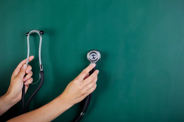 Woman's hands holding stethoscope against blackboard — Stock Photo, Image