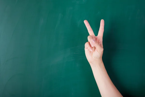 Woman's hand gesturing Victory sign against chalkboard — Stock Photo, Image