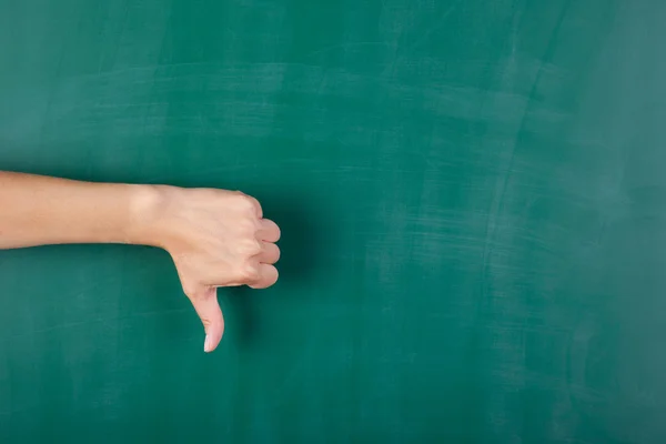 Woman's hand gesturing thumbs down against chalkboard — Stock Photo, Image