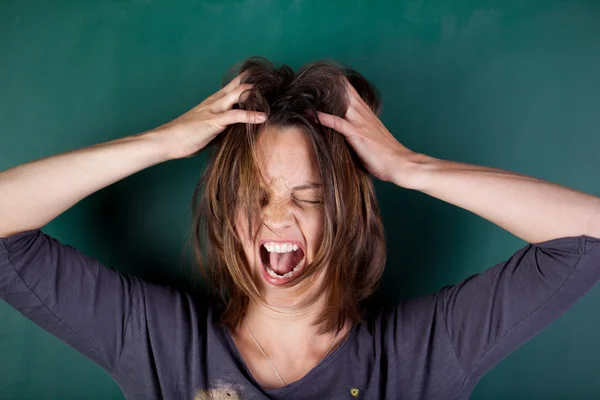 Frustrated woman with hands in hair screaming against chalkboard — Stock Photo, Image