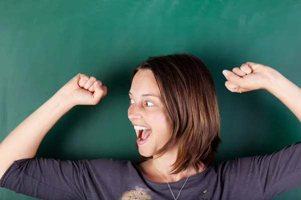 Woman with arms raised shouting against chalkboard — Stock Photo, Image