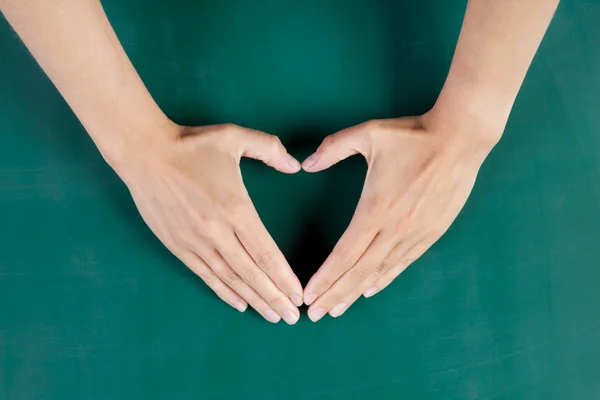 Frauenhände formen Herz gegen grünes Brett — Stockfoto