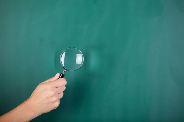 Woman's hand holding magnifying glass on green board — Stock Photo, Image