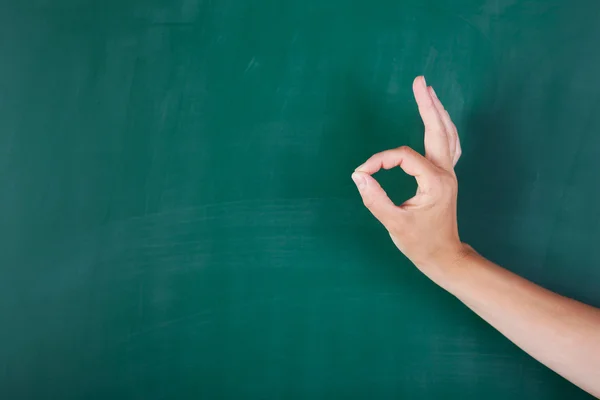 Vrouw hand gebaren Ok teken tegen schoolbord — Stockfoto