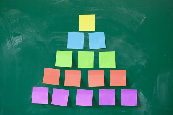 Colorful pyramid made of blank note papers stuck on blackboard — Stock Photo, Image