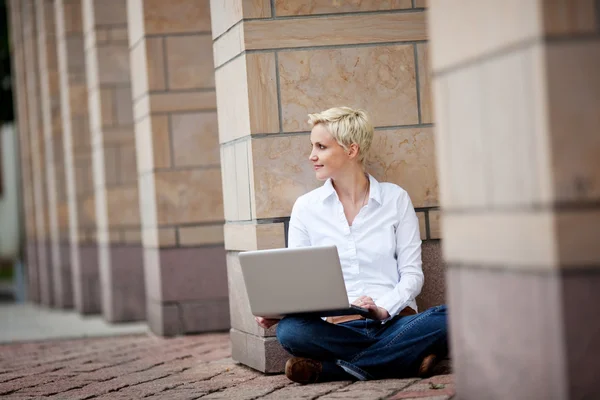 Donna con computer portatile seduto contro colonna — Foto Stock