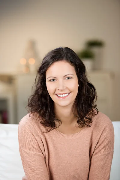 Młoda kobieta uśmiechając się siedząc na kanapie w domu — Zdjęcie stockowe