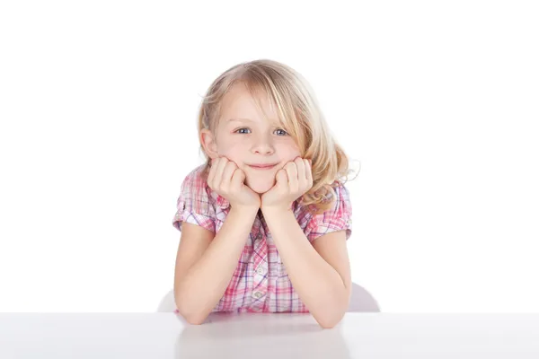 Meisje met hoofd in handen aan tafel tegen effen achtergrond — Stockfoto