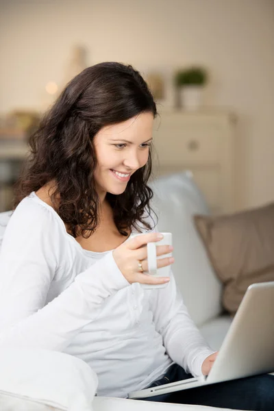 Mujer sosteniendo la taza de café mientras usa el ordenador portátil —  Fotos de Stock