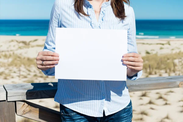 Woman showing white paper standing by the beach — Stock Photo, Image