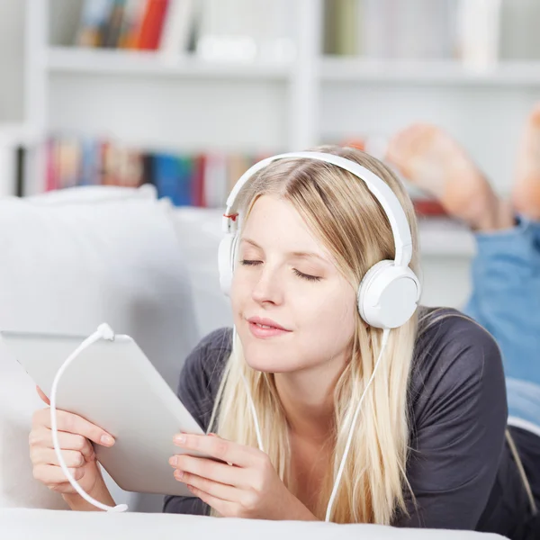 Kvinna njuter av musik i hörlurar med digital tablet på soffa — Stockfoto