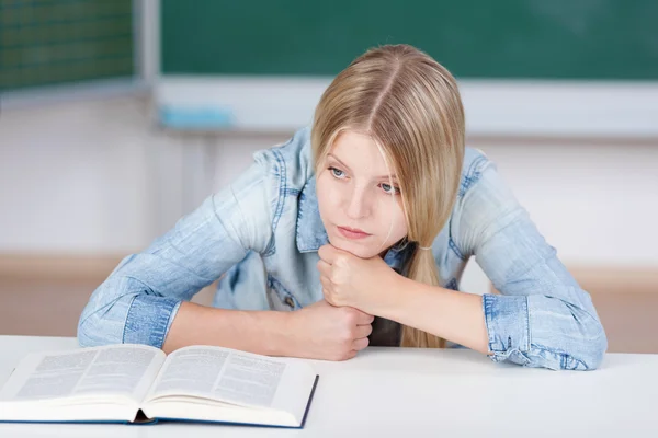 Student schaut weg, während er am Tisch studiert — Stockfoto