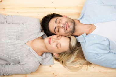 Couple With Eyes Closed Lying On Hardwood Floor clipart