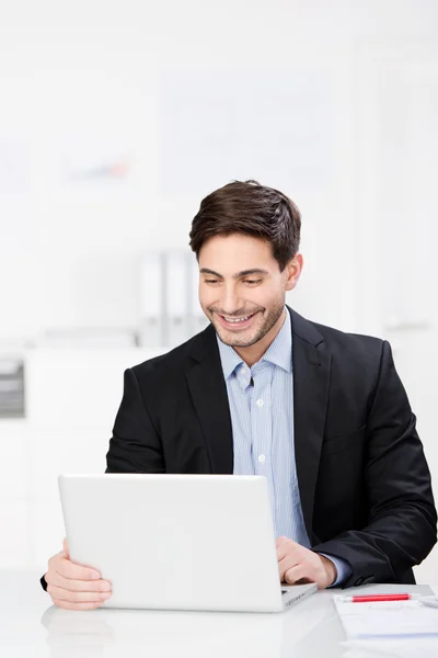 Smiling businessman seated at his laptop Stock Image