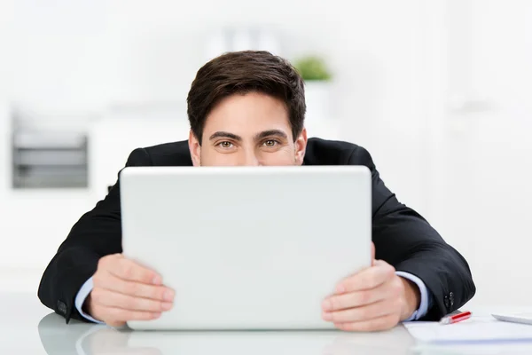 Uomo sorridente nascosto dietro il suo computer portatile — Foto Stock