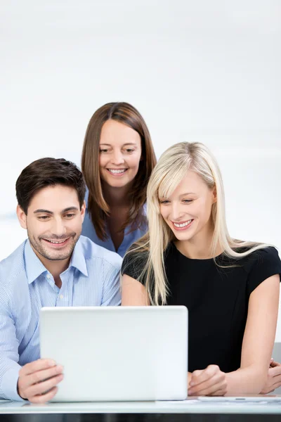 Compañeros de negocios sonriendo mientras leen un portátil —  Fotos de Stock