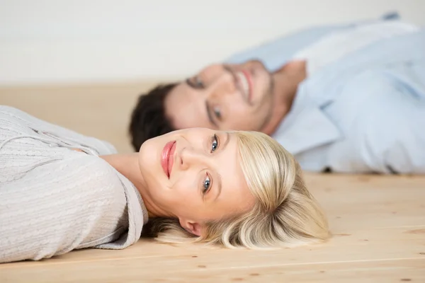 Mujer sonriendo con el hombre acostado en el suelo de madera —  Fotos de Stock