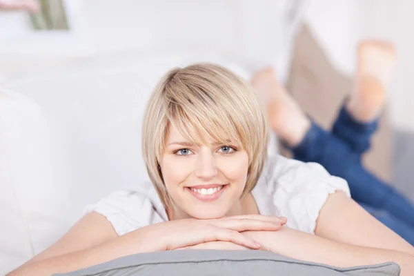 Vriendelijke blonde vrouw liggen op een sofa — Stockfoto