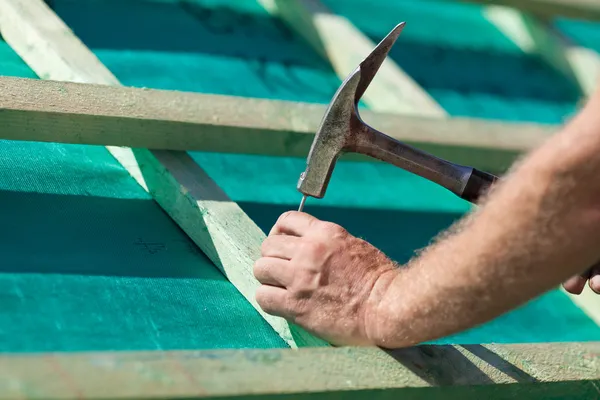 Roofer hammering a nail on the roof beams — Stock Photo, Image