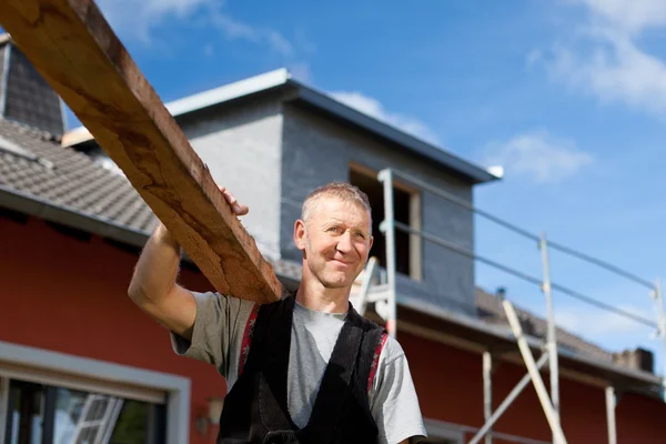 Roofer cargando una tabla de madera sobre su hombro — Foto de Stock