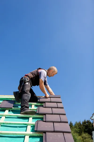 Roofer assembling gray tiles over the beams — Stock Image Roofer assembling gray tiles over the beams Royalty Free Stock Photos