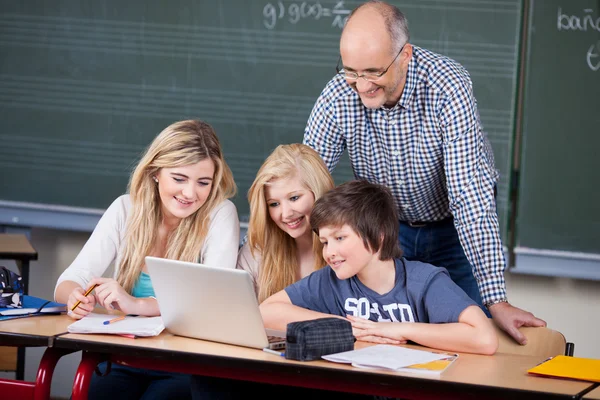 Студенты используют ноутбук, пока профессор смотрит на него за столом — стоковое фото