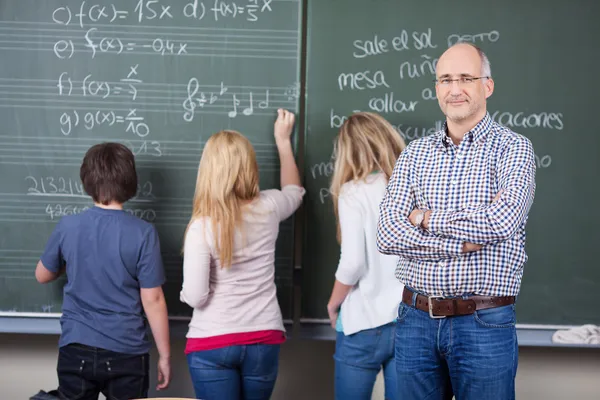 Insegnante maschio fiducioso con gli studenti che scrivono sulla lavagna — Foto Stock
