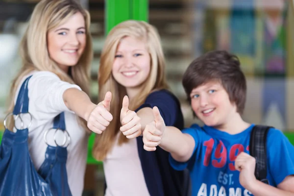 Счастливые ученики показывают пальчики вверх подписать вместе в школе — стоковое фото