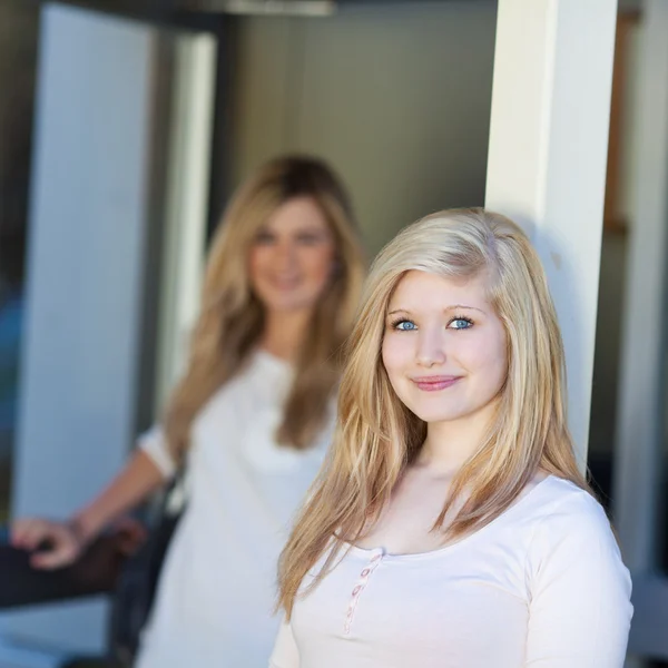 Adolescente chica sonriendo mientras amigo de pie en segundo plano — Foto de Stock