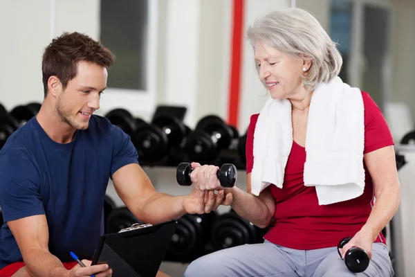 Instructeur aidant une femme âgée à soulever des haltères au gymnase — Photo