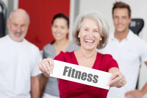 Starszy kobieta trzyma znak fitness z rodziną w tle — Zdjęcie stockowe