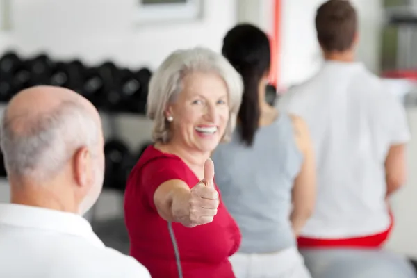 Donna gesturing pollice fino segno con famiglia seduta in palestra — Foto Stock