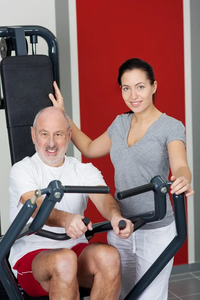 Instructor femenino con hombre mayor usando máquina de remo en el gimnasio — Foto de Stock