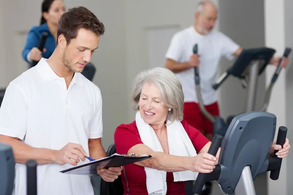 Instructeur expliquant l'horaire à une femme âgée au gymnase — Photo