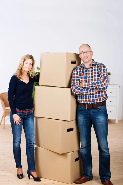Selbstbewusstes Paar steht vor gestapelten Pappkartons im neuen Zuhause — Stockfoto